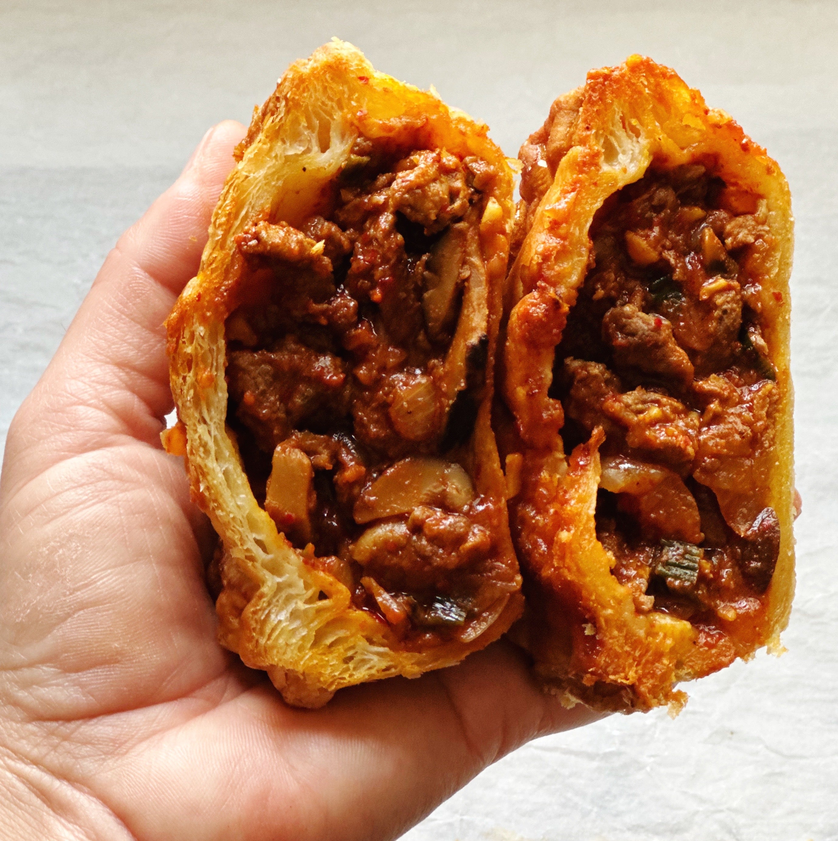 Hand holding a bake-at-home spicy korean-style steak pot pie featuring bold beef filling and a flaky puff pastry top