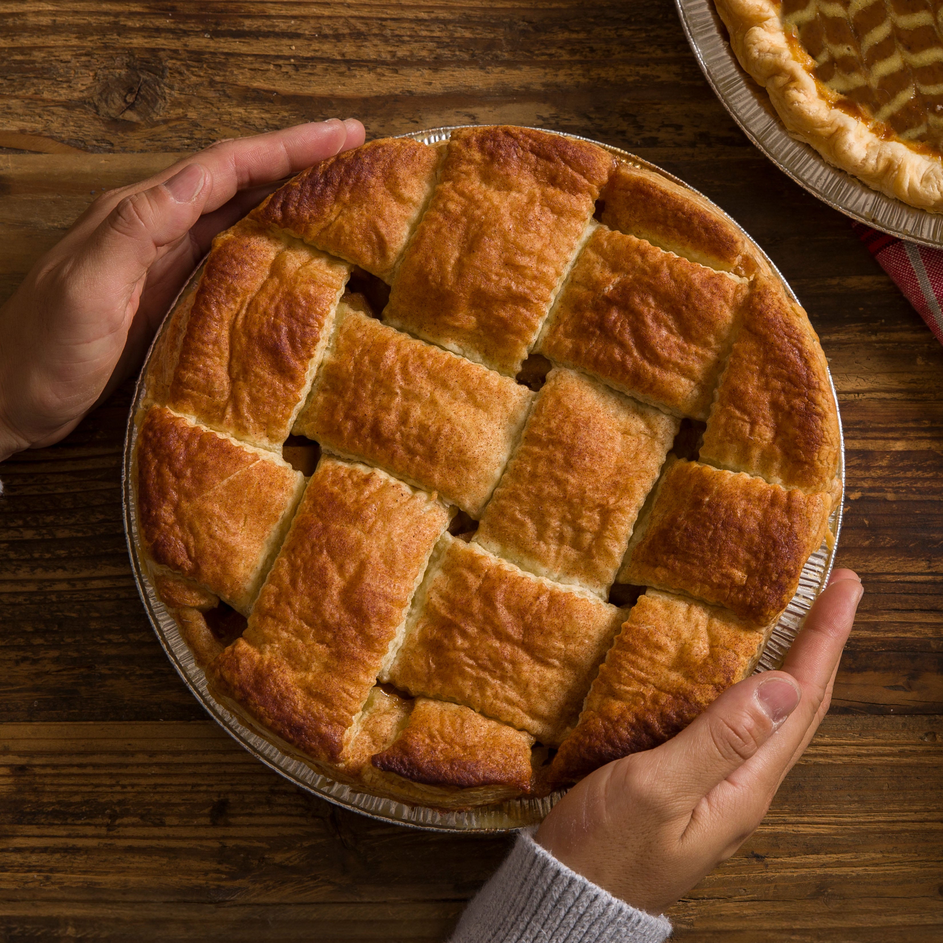 Hands holding and putting an apple pie onto a wooden table