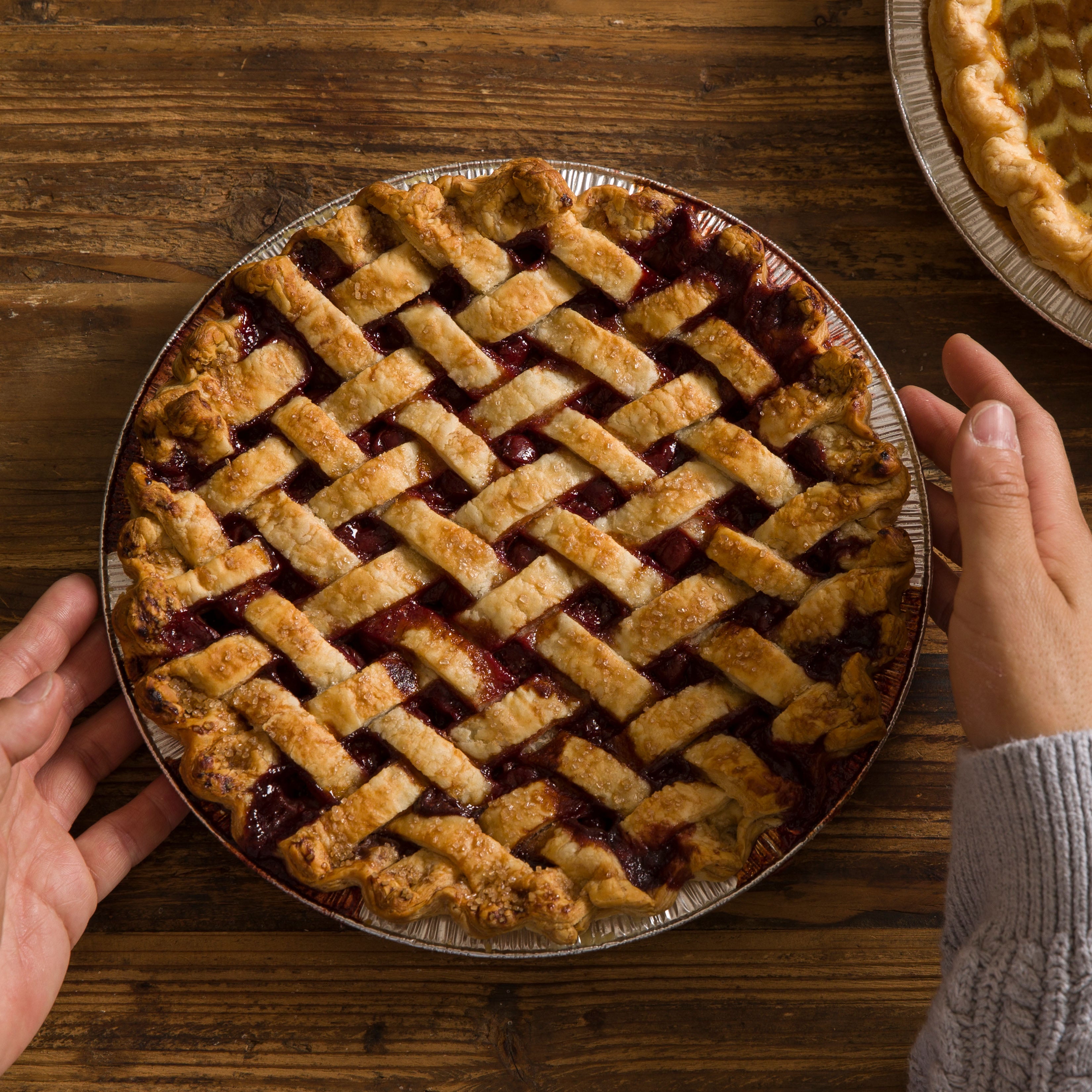 Hands putting a cherry pie with lattice work on wooden table