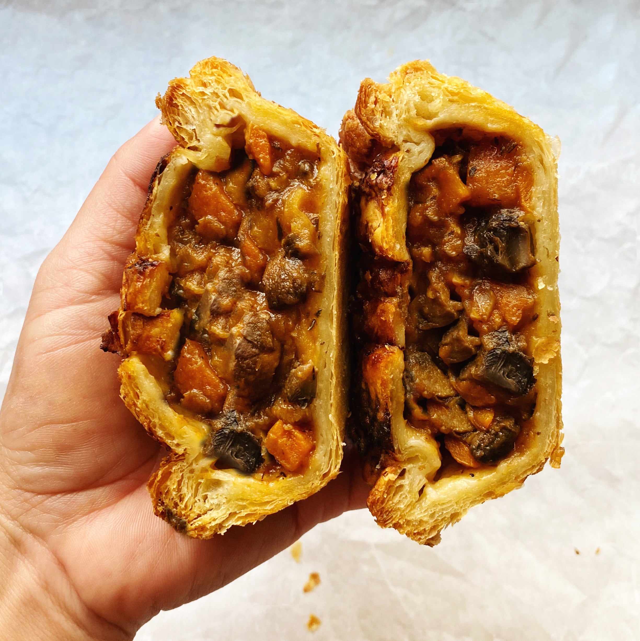Hand holding a bake-at-home savory vegan pot pie with a blend of mushrooms in a flaky puff pastry crust