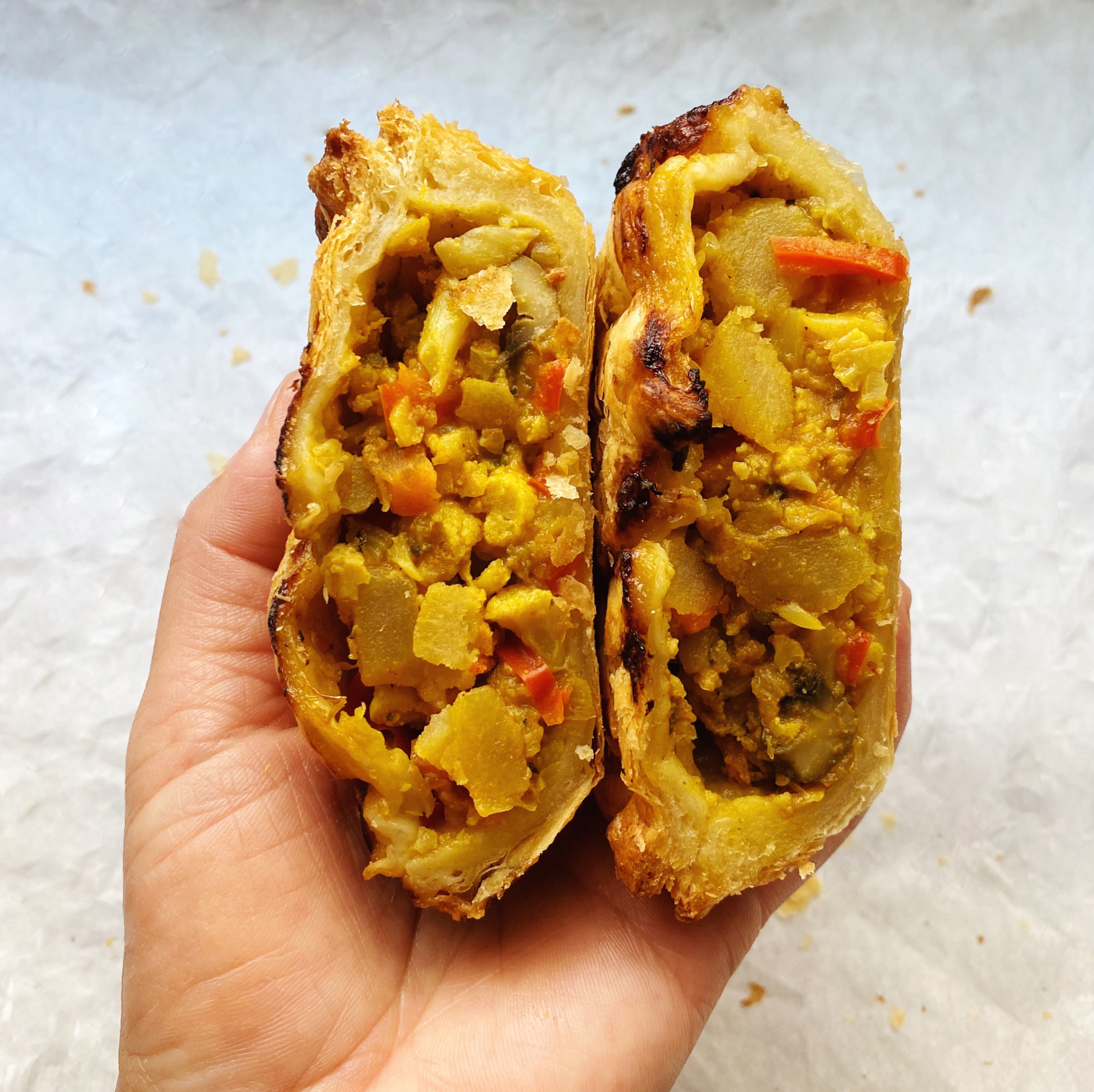 Hand holding a bake-at-home vegan vegetable curry pot pie wrapped in flaky golden puff pastry